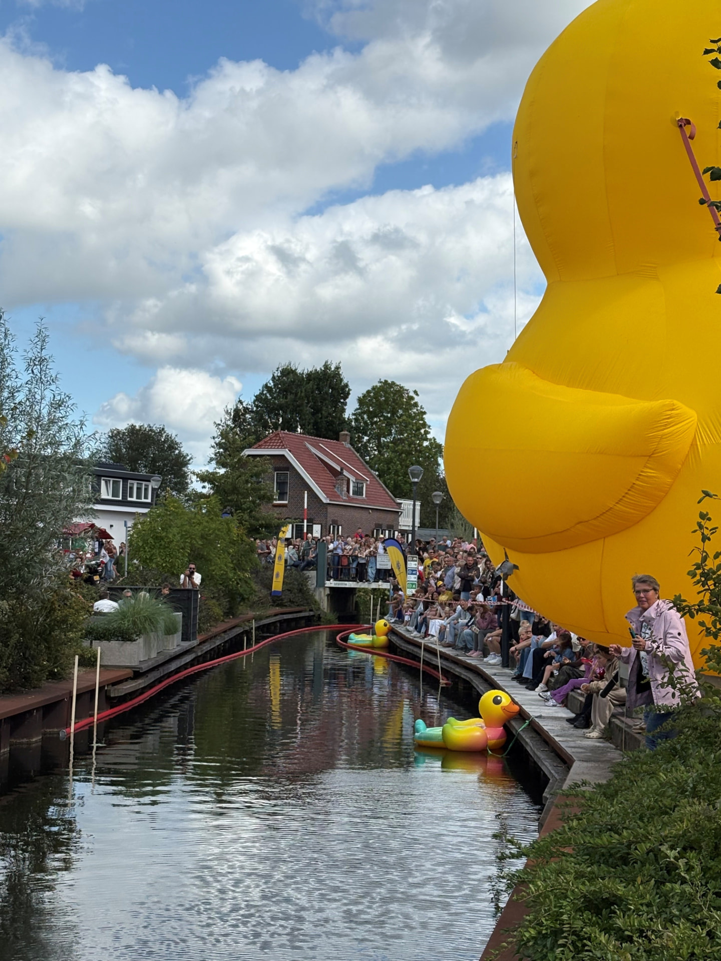 Opblaasbare reuze-eend langs de Hennipsloot met publiek op de kades tijdens de Badeendrace